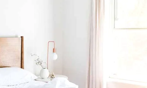 A white bedroom with a copper lamp and linen curtains.