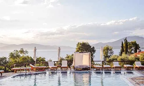 Sun loungers around a pool facing the sea at sunset.