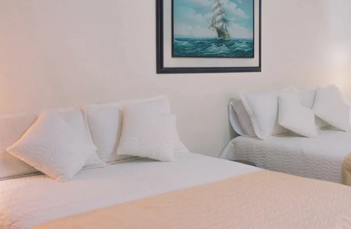 A white bed with many pillows under a painting of a ship at sea.