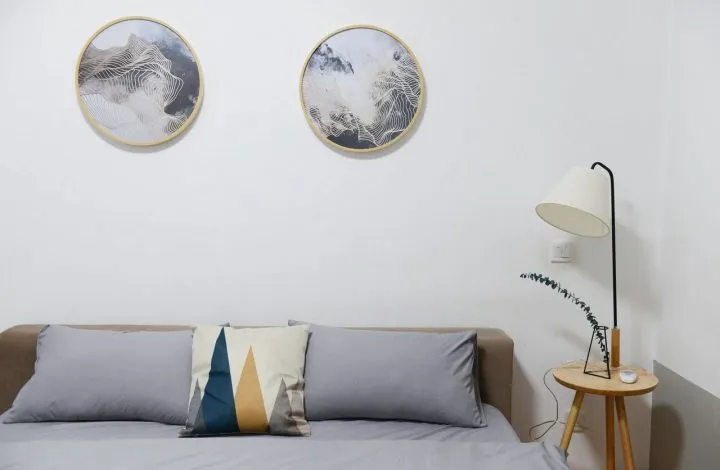 A white room with a grey sofa, two round prints and a floor lamp.