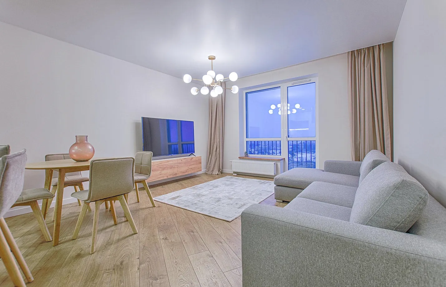 A living room with grey sofas, a dining table and a chandelier.
